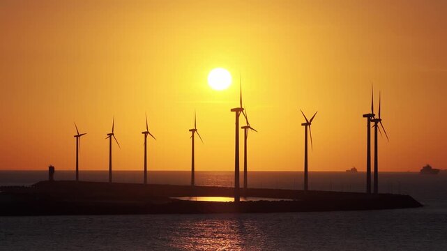 Aerial drone view of a wind generator at sunset over the sea and dam. Renewable energy infrastructure in evening light.