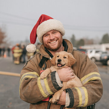 Smiling firefighter in santa hat holding cute golden retriever puppy outdoors during Christmas holidays