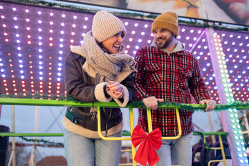 Obraz premium Cheerful young couple enjoying festival rides at a winter amusement park