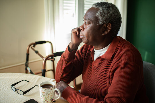 Senior man looking out window at table with walker
