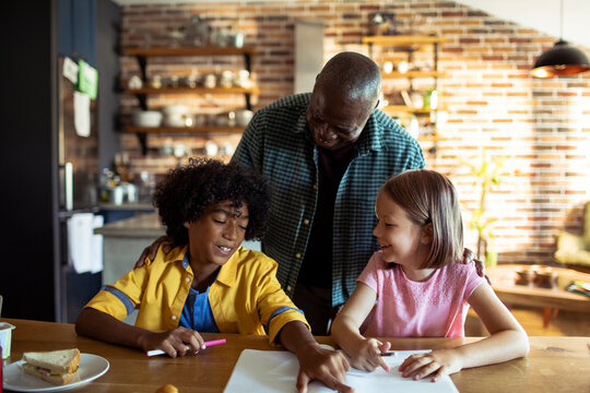 Older man helping two children with homework in kitchen