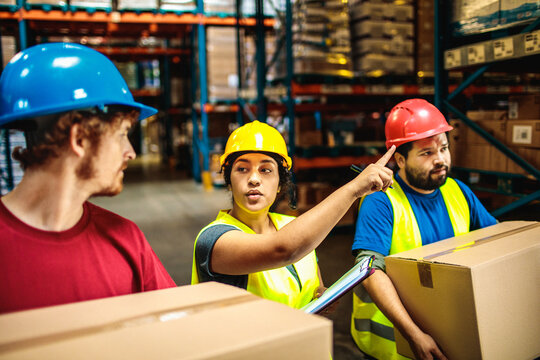 Warehouse supervisor directing workers carrying boxes