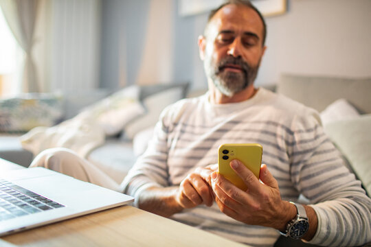 Middle-aged man using smartphone at home with laptop