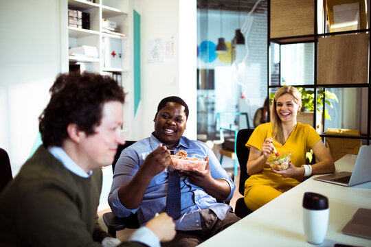 Coworkers eating lunch and laughing in office