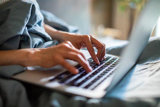 Hands typing on laptop in bed