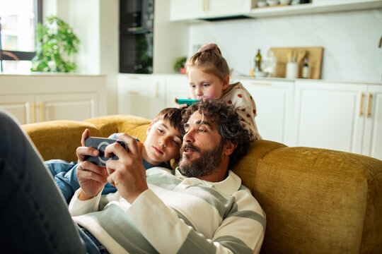 Father and kids looking at smartphone on sofa at home