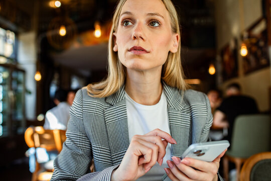 Businesswoman using smartphone while thinking in a cafe