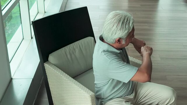 50s middle aged southeast asian man sitting in armchair, stretching arms to stay awake in living room, horizontal video