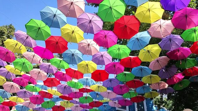 Hundreds of colorful umbrellas suspended above a street creating a vibrant canopy against blue sky. Urban art installation, festival decoration and city tourism attraction background.