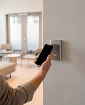 Hand tapping a smartphone against a wall-mounted RFID access reader at a coworking lounge