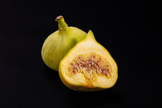 Fresh yellow fig cut in half showing pinkish seeds and creamy interior beside whole fig on black textured surface