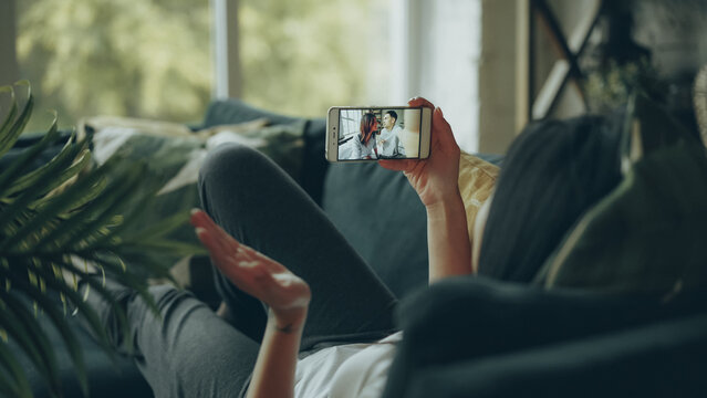 Female student is talking to friends beautiful couple online making video call with smartphone looking at screen and talking. Conversation and modern technology concept.