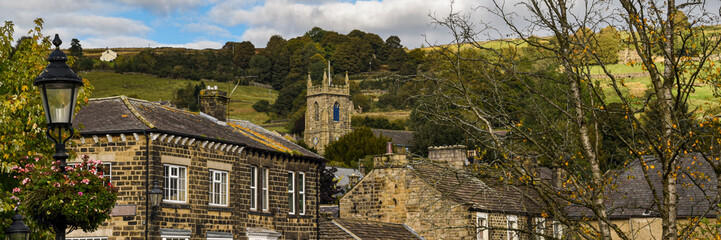 Traditional stone buildings and church tower in Pateley Bridge, North Yorkshire, surrounded by green hills beneath a dramatic cloudy sky in a classic English market town scene. © Gerard