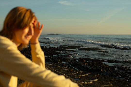 Out of focus woman in the foreground looking toward a rocky ocean coast with waves in sharp focus at golden hour