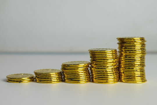 Stacks of gold coins arranged in ascending steps on a white background with copyspace idea for financial growth,,saving money and increasing wealth.