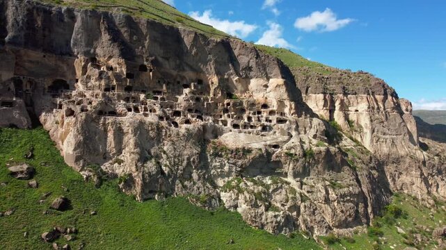 Aerial view moving alongside the ancient cave city of vardzia, a historic monastery complex carved into the erusheti mountain, showcasing its many levels and dwellings under a blue sky