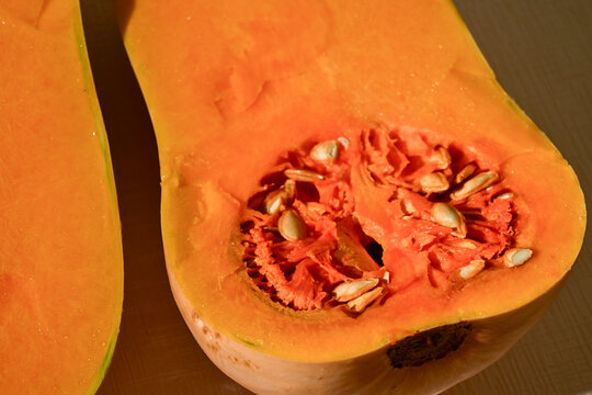 fresh cut butternut squash showing seeds and bright orange flesh on wooden surface