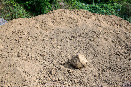 large pile of brown soil dirt for construction or gardening with green vegetation background outdoors