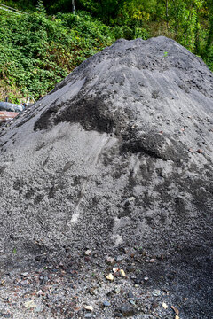 large pile of gray ash or industrial waste material outdoors near green vegetation
