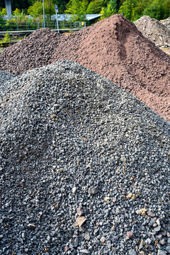 piles of construction gravel and sand outdoors at building site with green trees in background