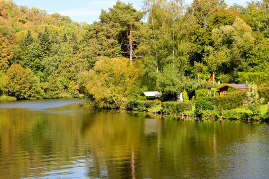 peaceful lake with green forest and small wooden cabin reflecting on calm water on sunny day