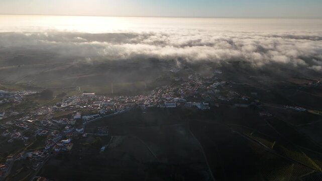 Aerial view of a town surrounded by rolling hills and low clouds during golden hour in Portugal.