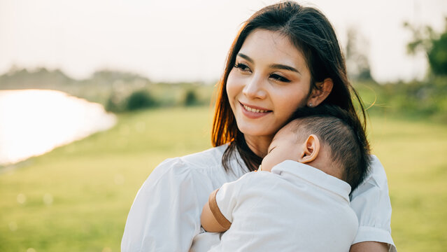 Happy beautiful mother holding baby sleeping son in the park