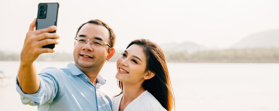 Asian Couple taking selfie picture with smartphone outdoor nature park, Happy smiling woman and man taking photo with mobile phone camera together
