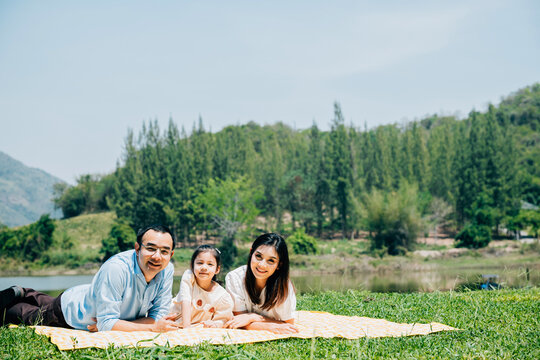 Asian family father mother and daughter lying on blanket spring meadow field grass in park cheerful sweet kid girl, parents and child picnic enjoying outdoors together