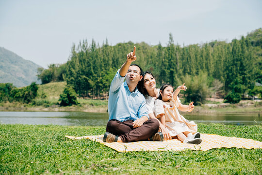 Asian family father mother and daughter sitting on blanket spring meadow field grass sunny day in park cheerful sweet kid girl, parents and child picnic enjoying outdoors together
