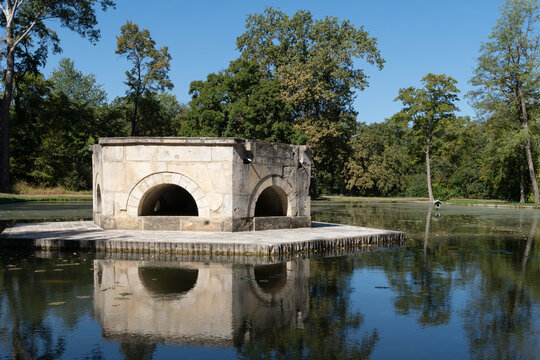 Stone structure with arched openings reflected in a pond