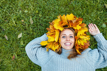 Obraz premium Portrait of a young woman wearing a handmade maple leaf wreath in an autumn park. Fall leaves, seasonal lifestyle, outdoor wellness and colorful foliage create a cozy autumn portrait.
