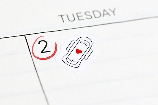 Close up of calendar with sticker showing sanitary pad and red heart. Reminder for tracking menstrual cycle and period start