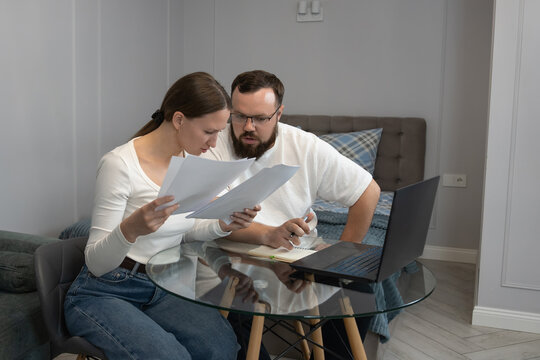 Couple reviewing financial documents, managing personal budget, and using a laptop in their home, indicating financial stress and serious discussions about debt or bills