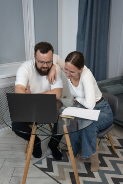 Happy couple smiling and discussing important documents while working from home, sharing a laptop and celebrating success on a financial or project review. Vertical photo