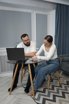 Couple reviewing paperwork and discussing financial planning at a glass table in their home, using a laptop for online banking and managing household budget. Vertical photo