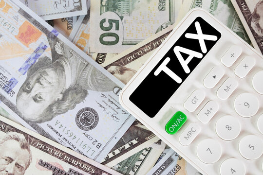 White calculator with TAX text on the display resting on scattered US dollar bills idea fortax payment, business accounting, financial planning.