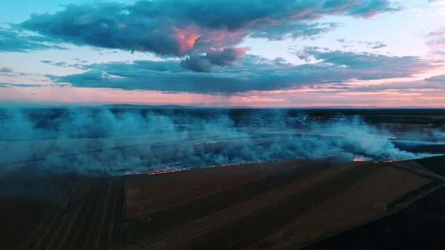 Aerial view of a field burning at sunset with smoke rising over the agricultural landscape in Sremska Mitrovica, Vojvodina, Serbia.