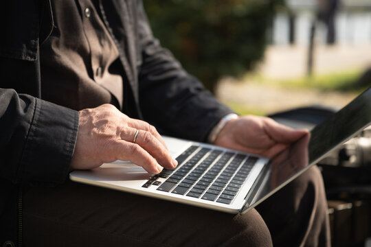 Close up of a man using a laptop while sitting outdoors in sunlight, illustrating remote work, mobile office, freelance job and flexible workplace.