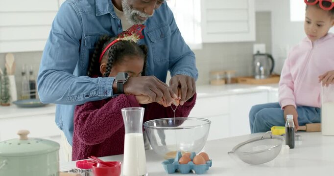 African man guiding hands of youth girl at kitchen island, cracking eggs into bowl