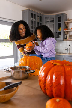 African American mother and youth daughter carving halloween pumpkins at counter with steel pot