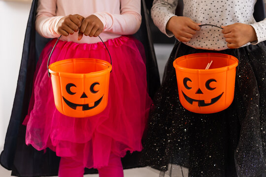 Two female African American children holding pumpkin buckets at home for halloween wearing tutus