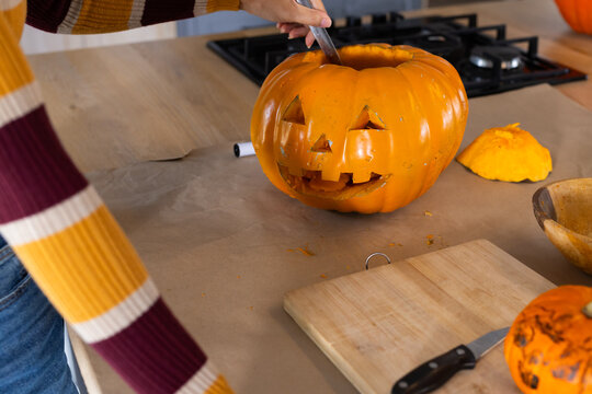 Bright pumpkin is being carved on craft paper countertop with knife and lid, halloween