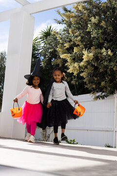 African American girls walking hand in hand on porch by pergola carrying pumpkin buckets halloween