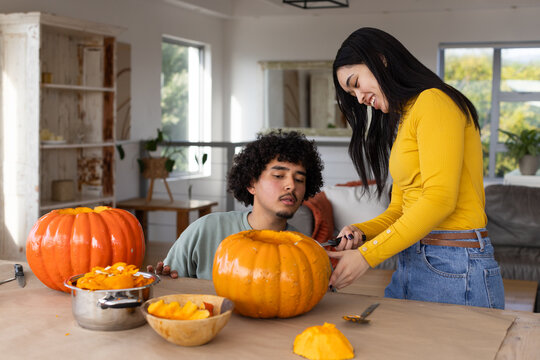 African American couple woman in yellow top carving halloween pumpkins at home with knife pot bowl