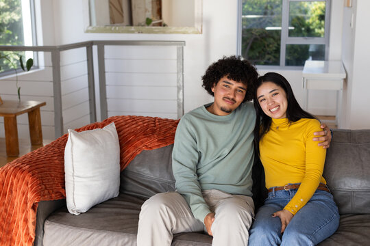 Couple sitting on gray leather sofa at home by window wearing green sweatshirt and yellow top