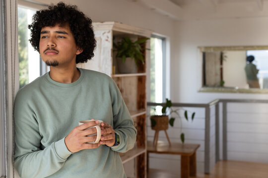 African American man sage top with watch leaning on window holding mug gazing outside, copy space