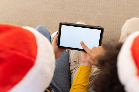African American couple wearing christmas hats pointing at black tablet with blank screen on carpet