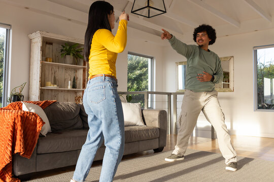 African American couple dancing playfully in bright living room near gray sofa and orange throw