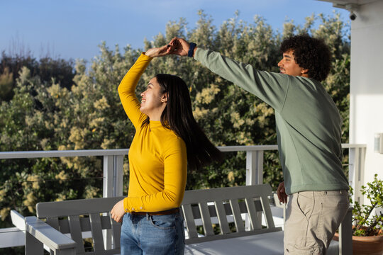 African American couple dancing on covered balcony by bench, woman mustard top, man sage pullover